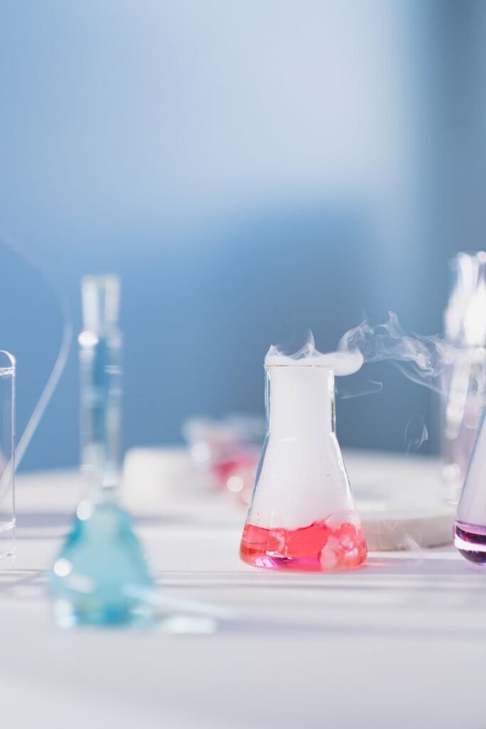 Erlenmeyer flasks emitting steam with colorful liquid in a lab setting.